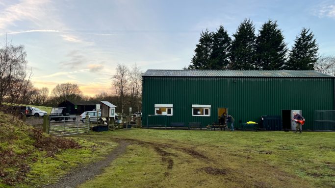 A green building in a rural area with people and trees at sunset.