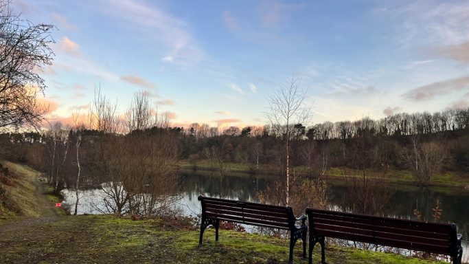 Serene lakeside scene with two benches and a sunset sky.